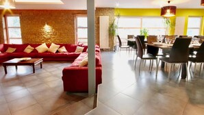 A modern living room with a red sofa, a dining area with a table and chairs, and a stone wall. - Holiday Home in Stoumont With Private Sauna (Stoumont)