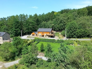 A two-story house with a stone facade and wooden accents, surrounded by lush greenery and a hillside. - Holiday Home in Stoumont With Private Sauna (Stoumont)