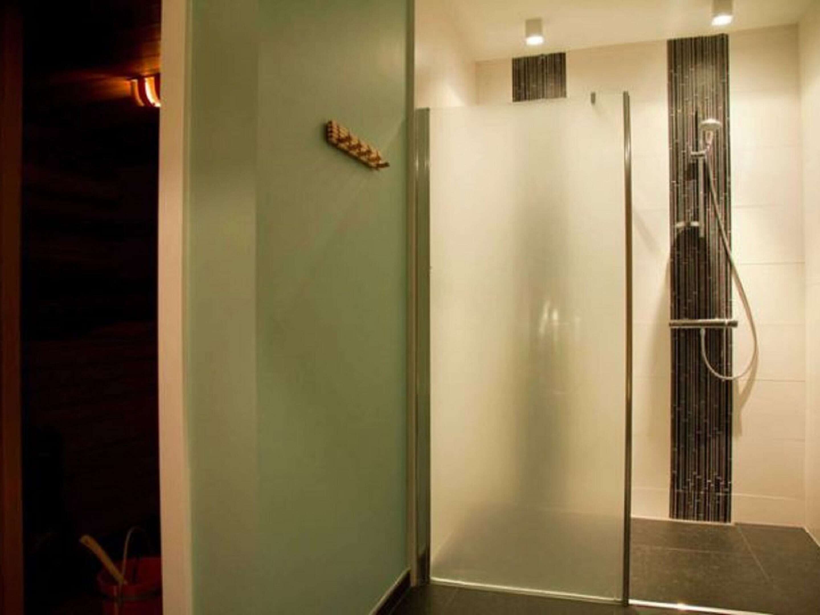 A modern bathroom with a glass-enclosed shower, a small shelf with toiletries, and a dark floor.