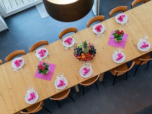 A long wooden dining table set for a meal with pink napkins, clear glasses, and a centerpiece of fruit and flowers. - Comfy Home with Sauna Located near Forest (Waimes)