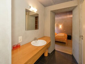 A bathroom with a wooden vanity, a white sink, and a mirror. There is a small trash bin under the sink and a light fixture above the mirror. - Comfy Home with Sauna Located near Forest (Waimes)