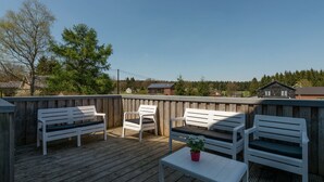 A wooden deck with white benches and a table, surrounded by a wooden fence, overlooking a residential area with houses and trees. - Comfy Home with Sauna Located near Forest (Waimes)