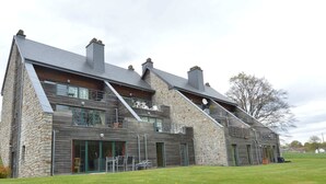 Une maison moderne à deux étages, dotée d’une façade en pierre, de grandes fenêtres et d’une vaste pelouse à l’avant.