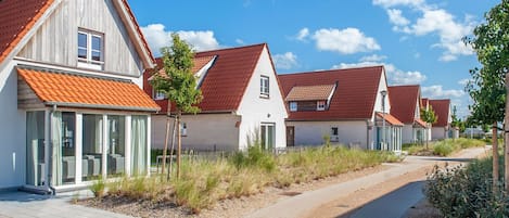 Eine Reihe moderner Häuser mit roten Ziegeldächern und großen Fenstern, ein gepflasterter Weg und ein klarer, blauer Himmel.