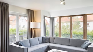 A modern living room with a grey sectional sofa, a white coffee table, and large windows offering a view of the outside. - Villa, two Bathrooms and a Washing Machine, Near Ostend (Bredene)