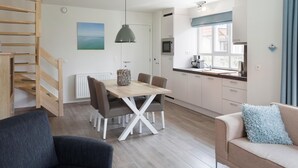 A modern kitchen with white cabinets, a dining table with chairs, a staircase, and a sofa with a cushion. - Villa, two Bathrooms and a Washing Machine, Near Ostend (Bredene)