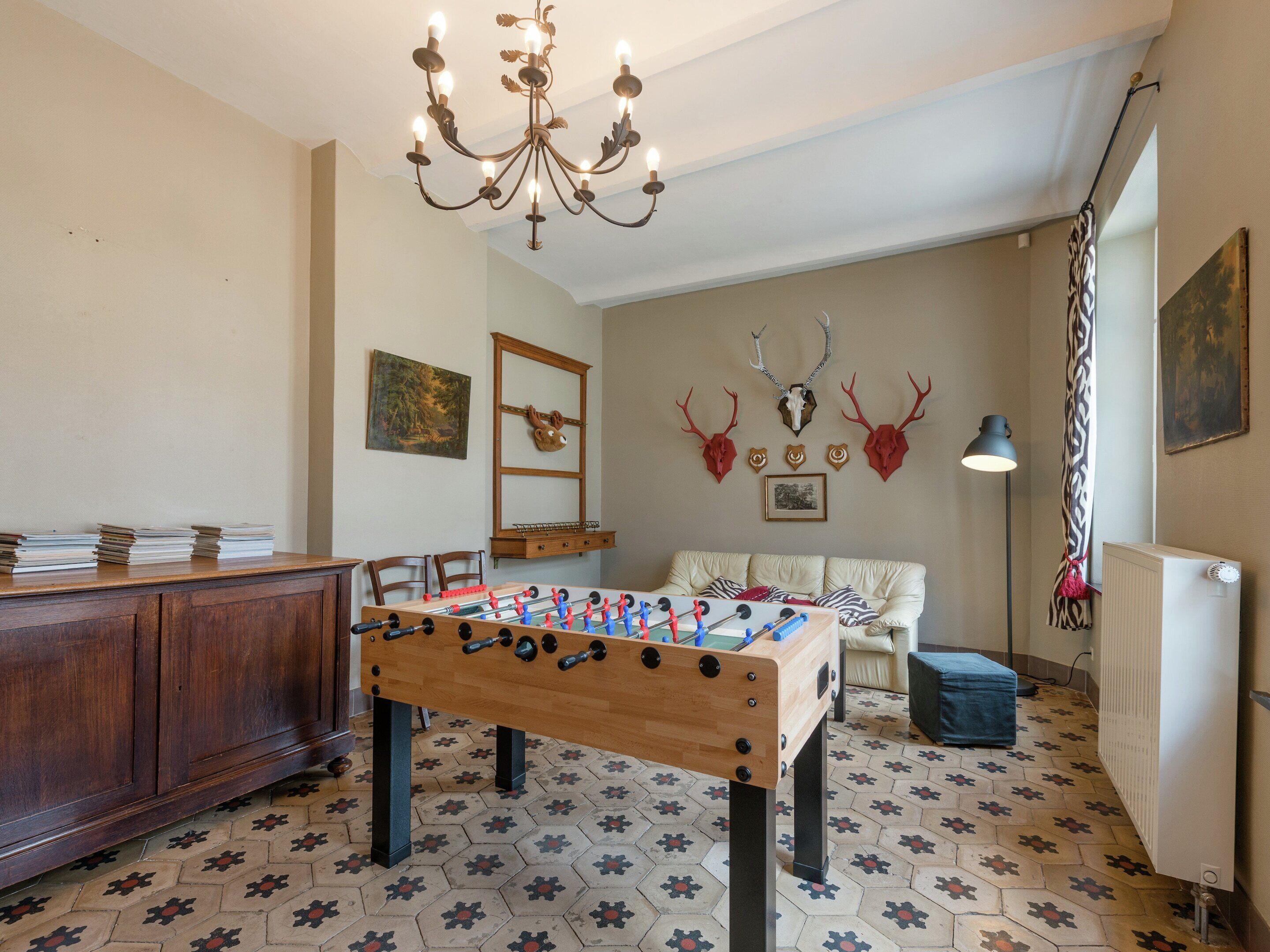 A room with a wooden foosball table, a chandelier, and wall-mounted deer skulls.