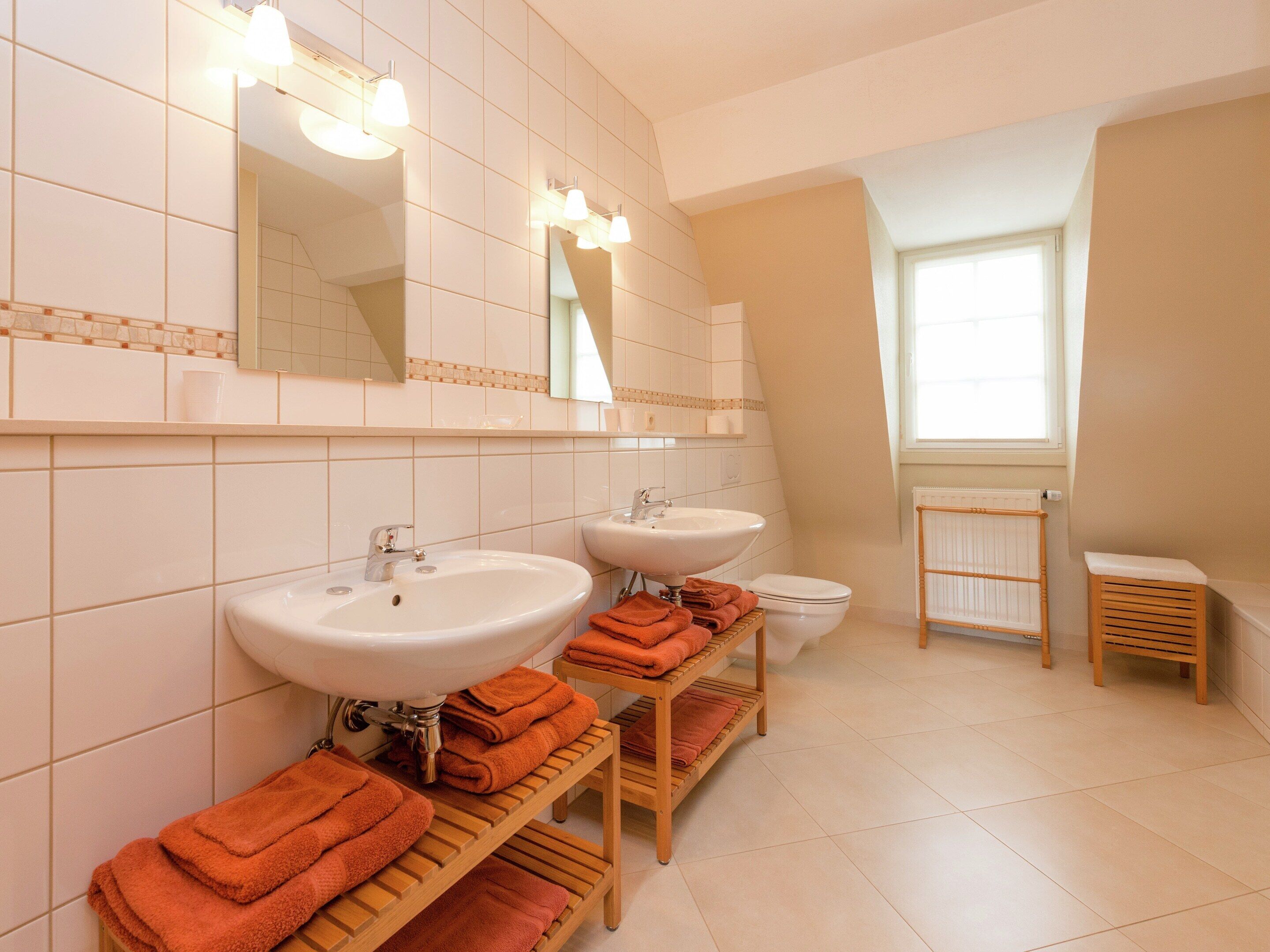 A modern bathroom with two sinks, a toilet, and a window.