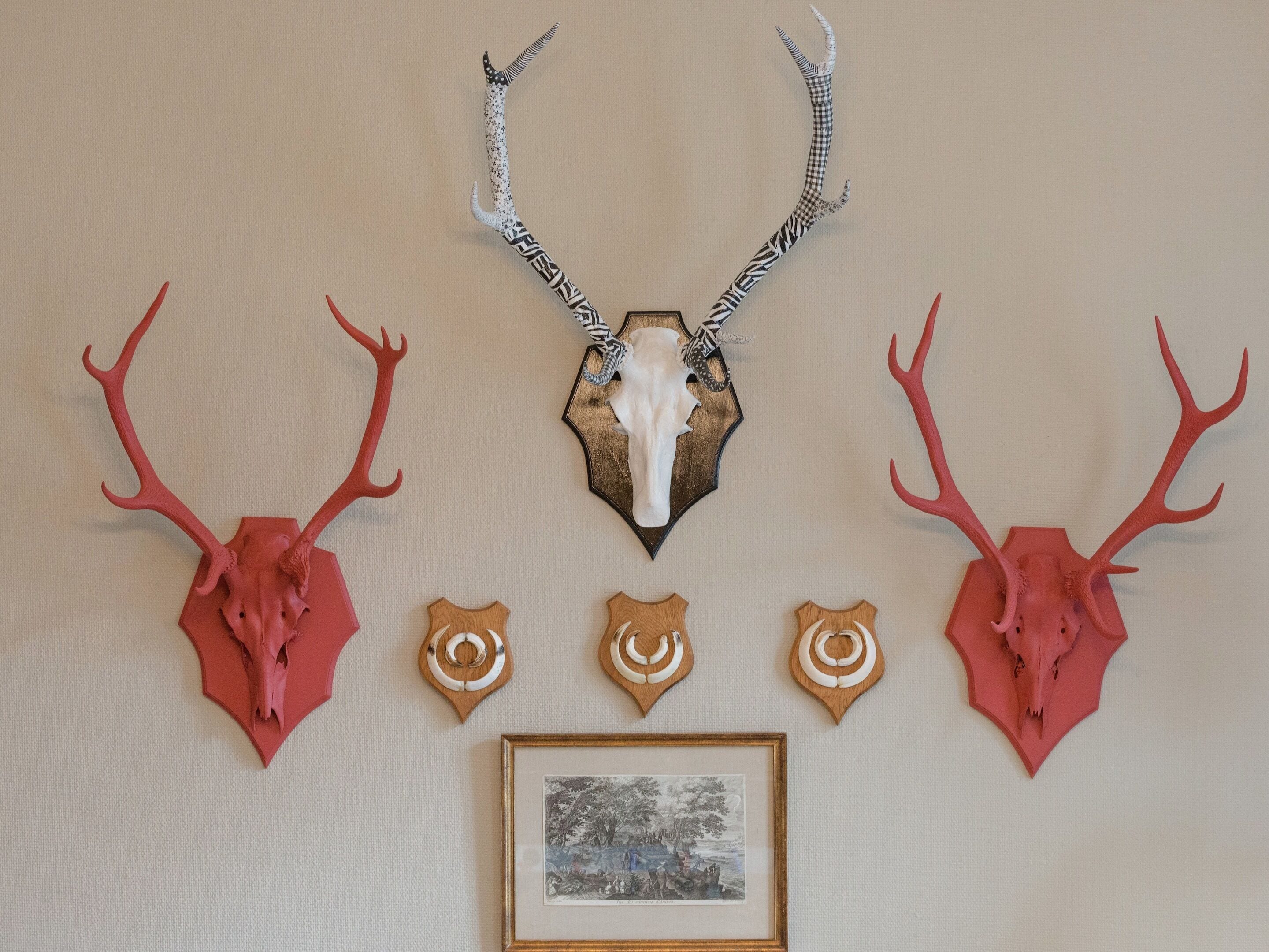 A wall with mounted animal skulls and antlers, a framed picture, and decorative wooden shapes.