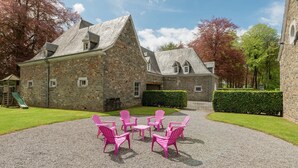 A stone building with a gravel courtyard, pink Adirondack chairs, and a playground.