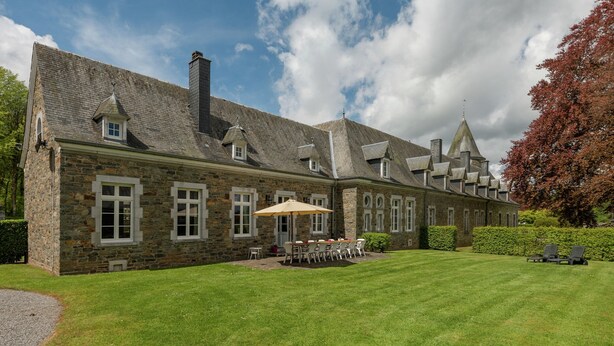 A stone building with multiple windows and a lawn area with outdoor seating.