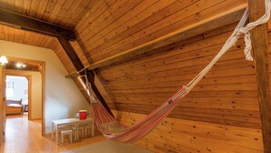 A hammock in a wooden room with a sloped ceiling, a small table, and a chair.