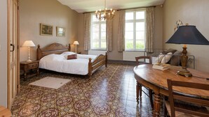 A bedroom with a large bed, two bedside tables, a chandelier, a dining table with chairs, and a patterned floor.