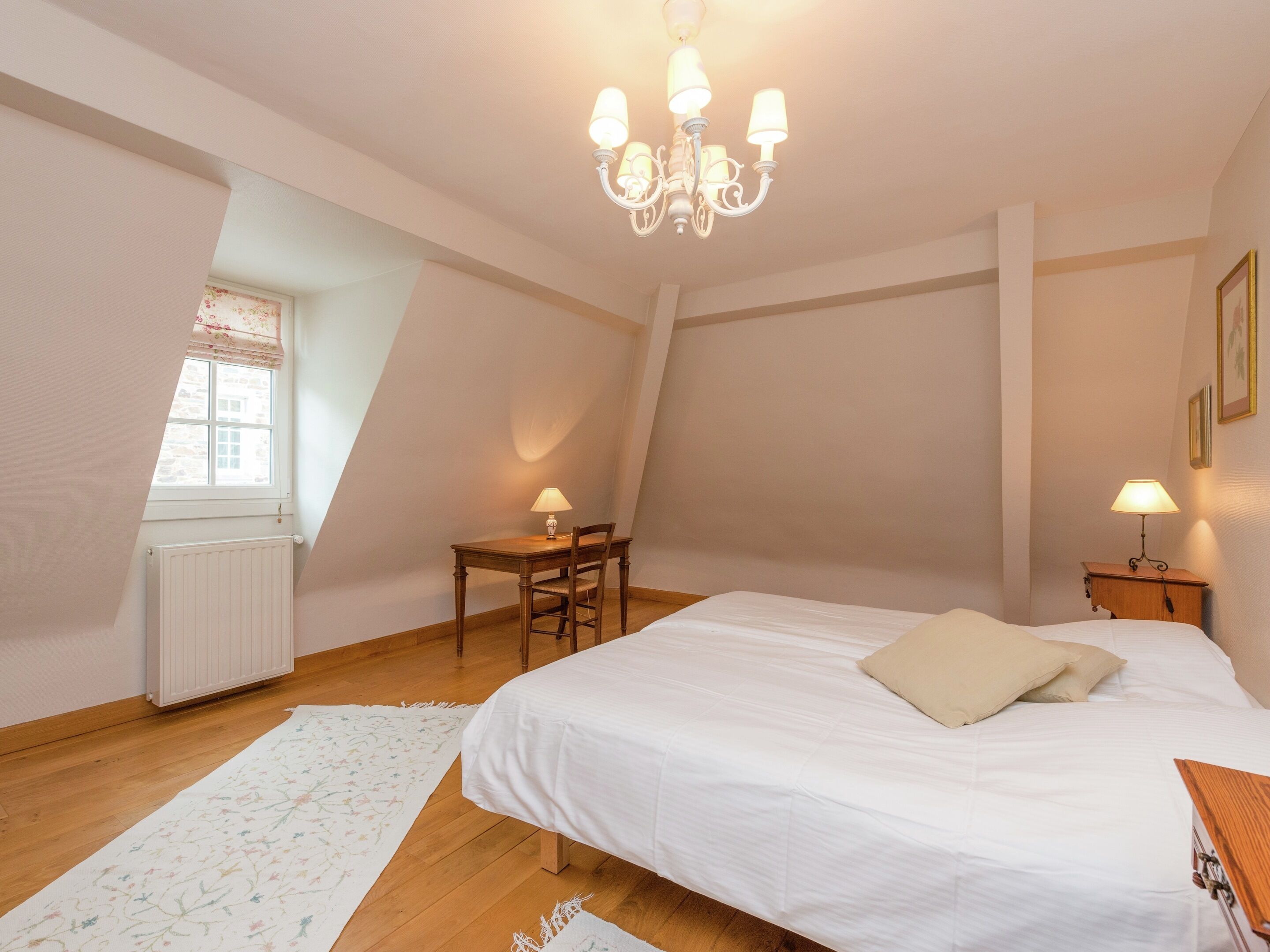 Un dormitorio con una cama grande, un escritorio y una silla. Se ve una ventana con vistas al exterior.