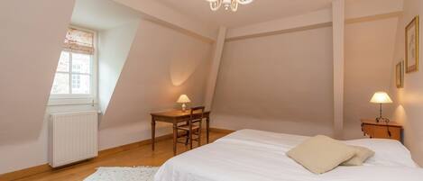 Un dormitorio con una cama grande, un escritorio y una silla. Se ve una ventana con vistas al exterior.