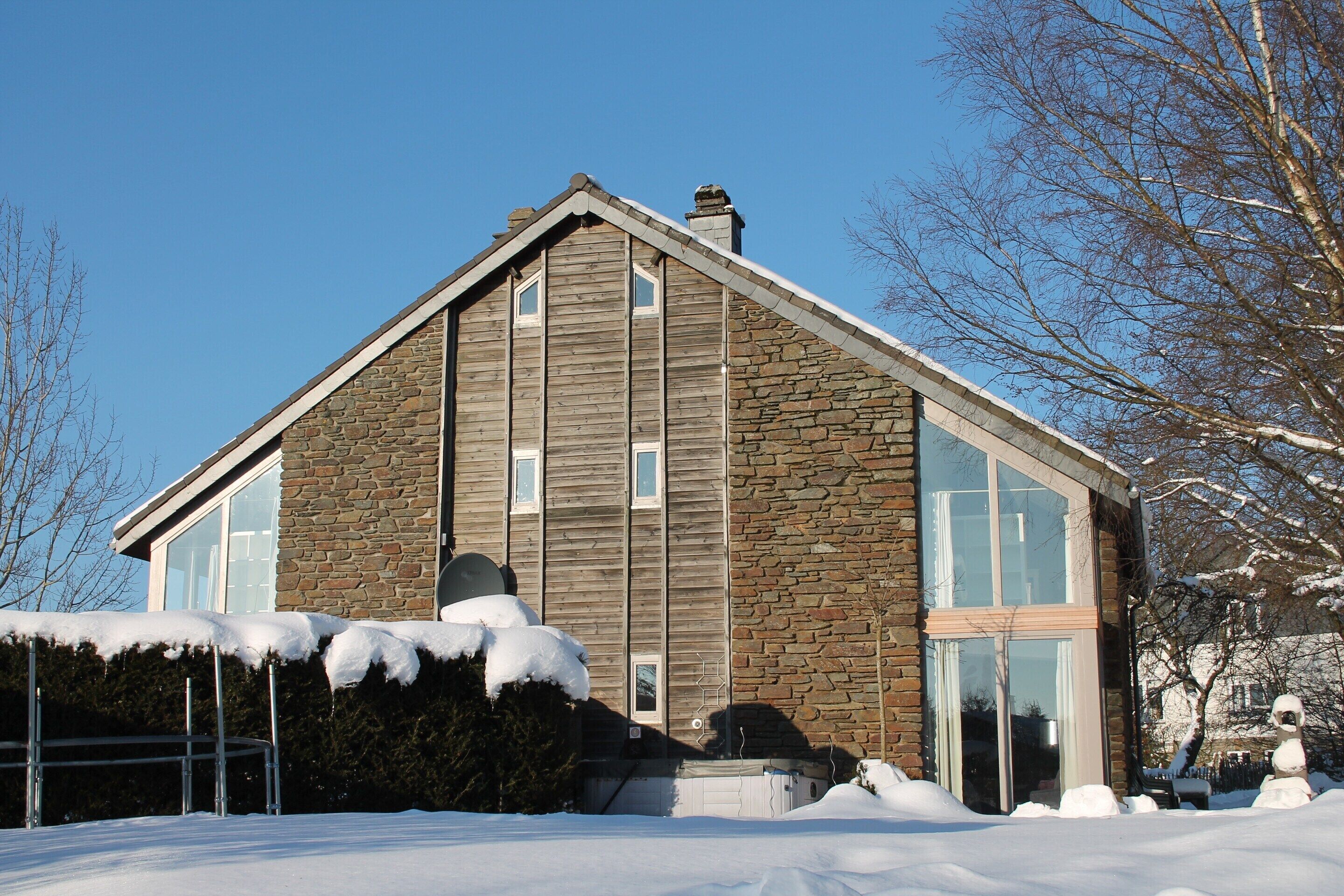A modern house with a stone facade and large windows, surrounded by snow.