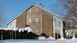 Ein modernes Haus mit Steinfassade und großen Fenstern, umgeben von Schnee.