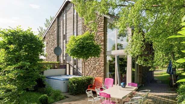 Ein modernes Haus mit Steinaußenwand, einer Holzterrasse und einer Terrasse mit Gartenmöbeln.