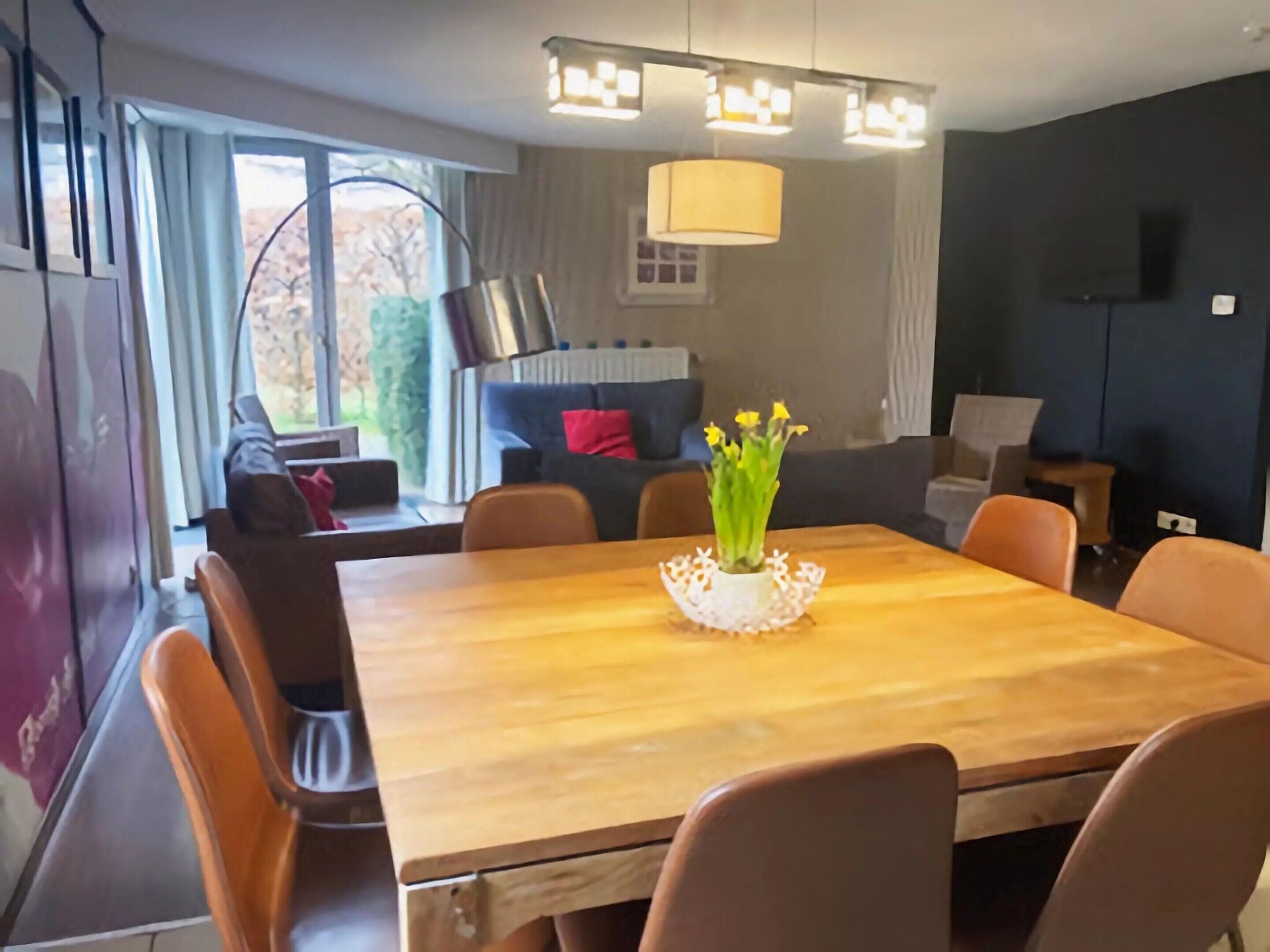 Un espace de repas moderne avec une table et des chaises en bois, un vase rempli de fleurs et un canapé en arrière-plan.