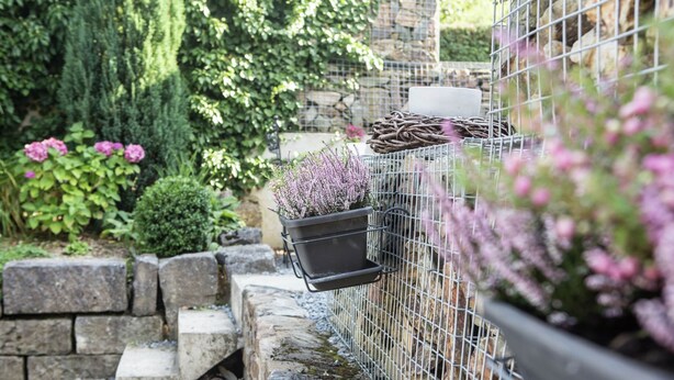 Een tuin met een stenen muur, een metalen hek en bloempotten.