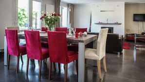 Een moderne eethoek met een houten tafel, rode fauteuils en een bloevas.