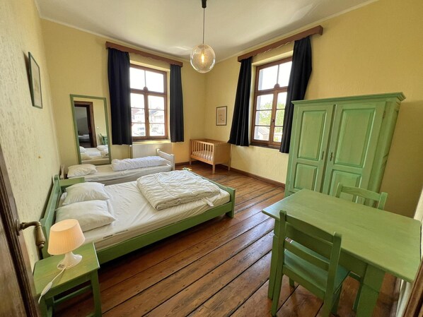 A room with two beds, a wooden floor, a green table, and a green chair.