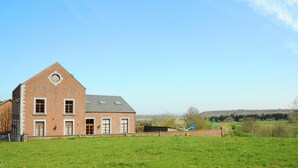 A brick building with a triangular roof, a playground, and a green field in the foreground. - House near Caves of Hotton, L' Ourthe, & Durbuy (Somme-Leuze)