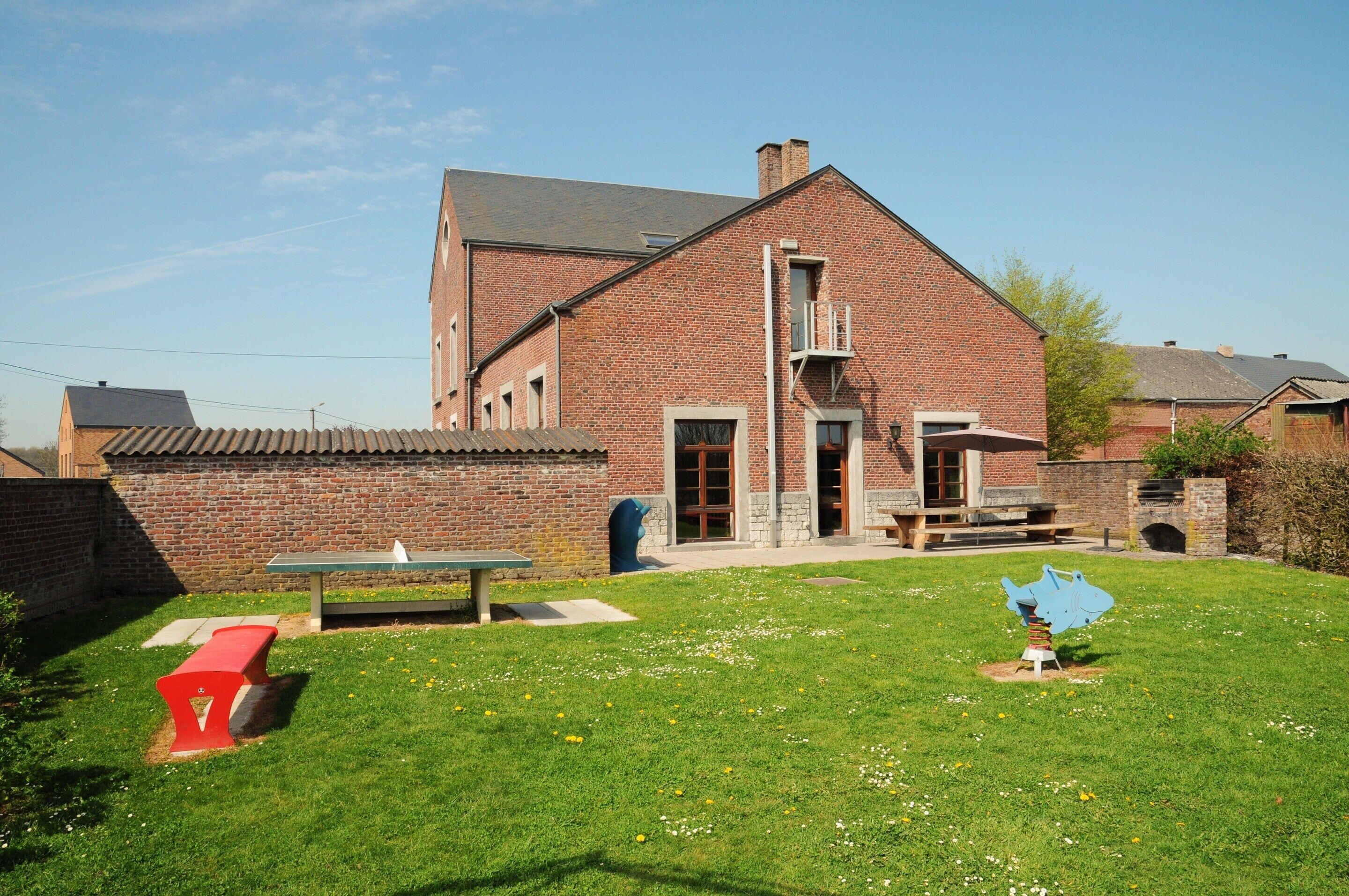 A brick building with a sloped roof, a front door, and a small front yard with a bench and a sculpture.
