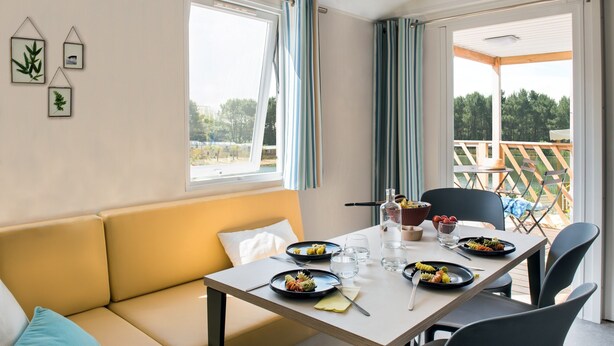 Un coin repas avec une table dressée pour deux personnes, un canapé et une vue sur l’extérieur.