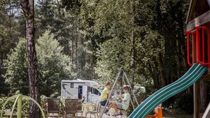Un terrain de camping équipé d’une balançoire, d’un toboggan vert et d’un espace repas avec des chaises et des tables.
