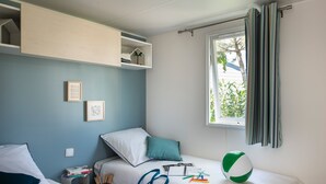 Une chambre avec un lit, une fenêtre avec des rideaux, une étagère avec des livres et un ballon de plage.