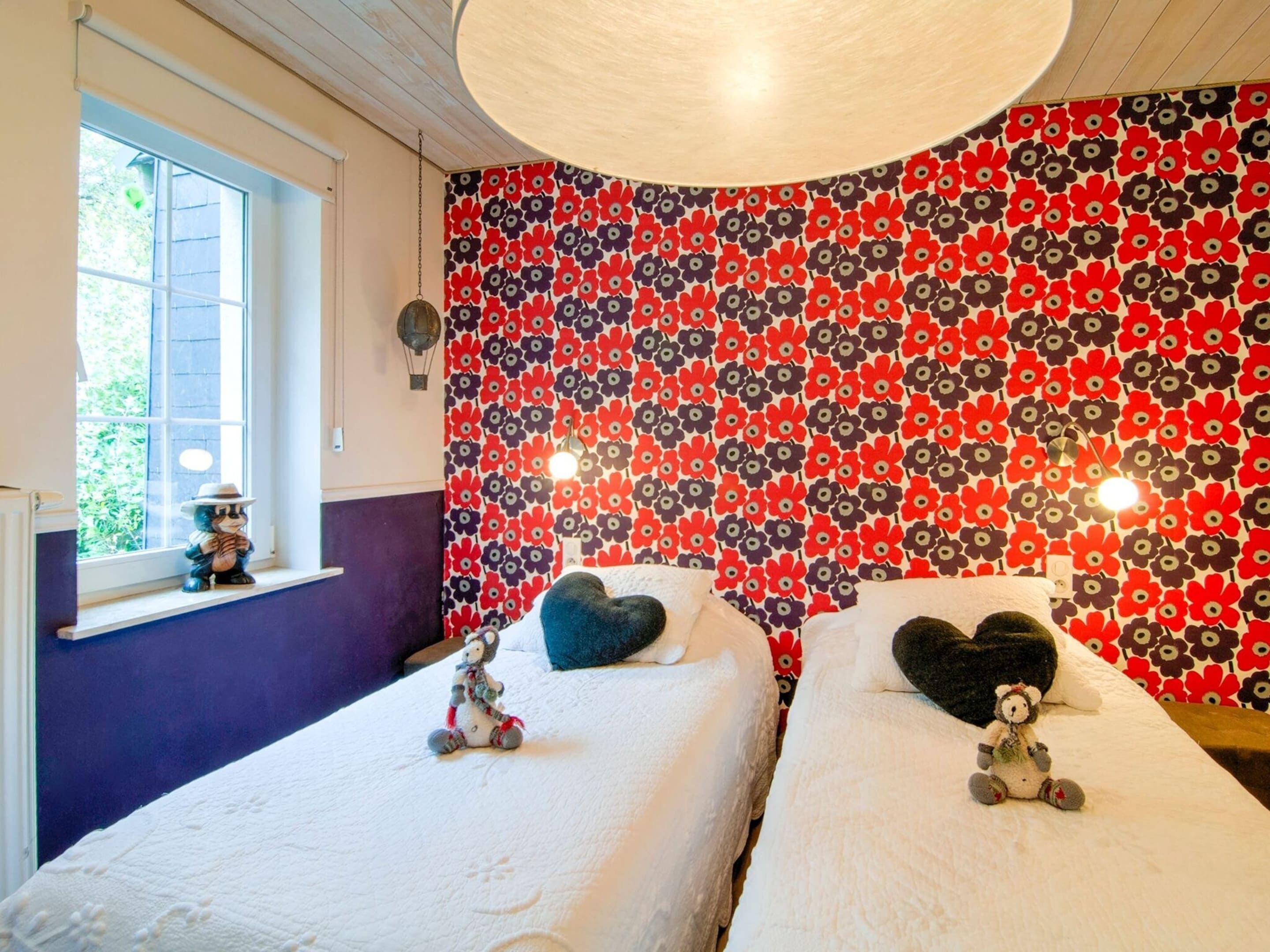 A bedroom with two beds, a window, and a floral-patterned wall.