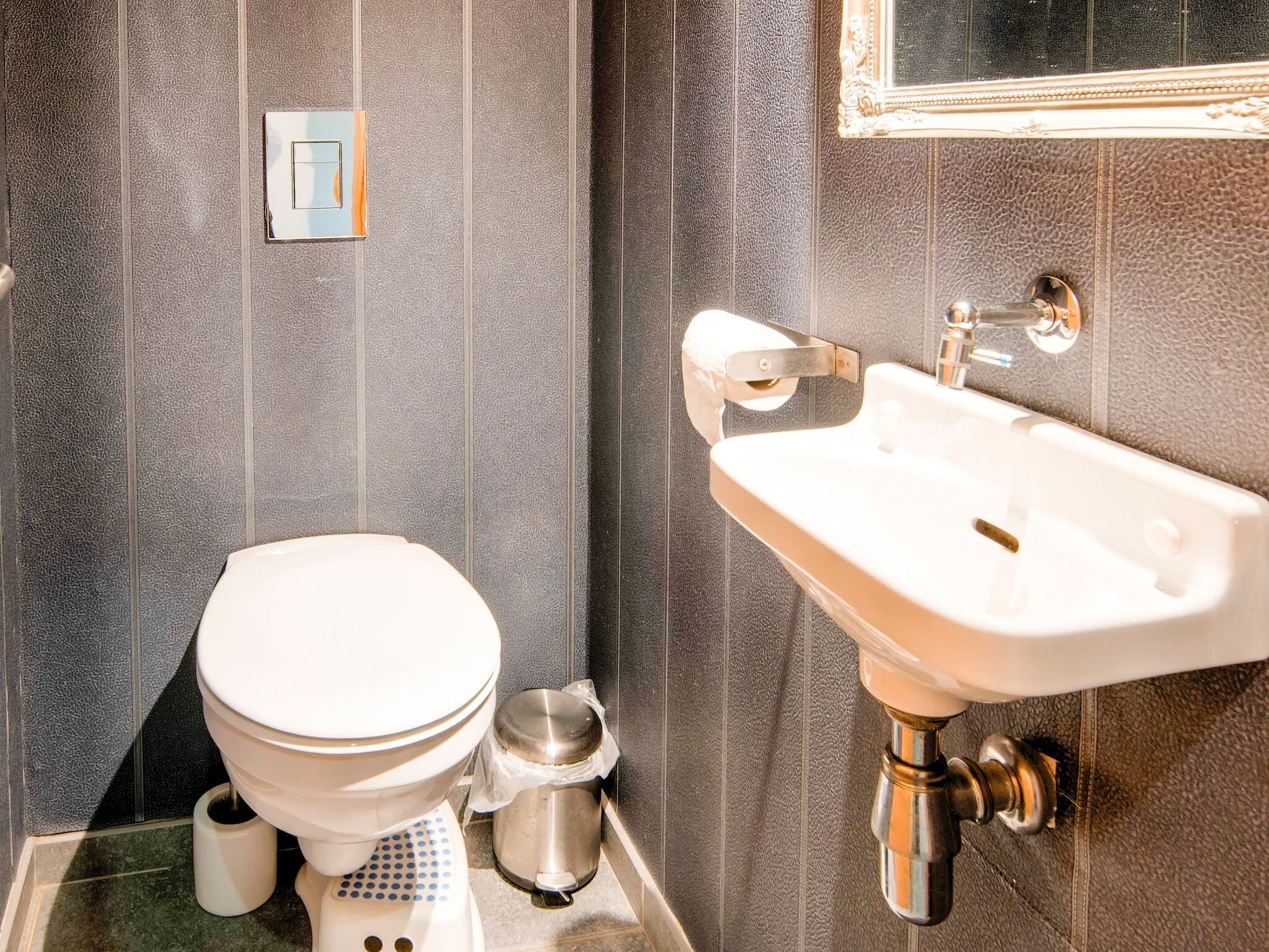Un baño con inodoro, lavamanos y un cubo de basura.