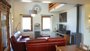 A living room with a sofa, a dining table with chairs, a TV, and a fireplace. - Stone House in Durbuy With Sauna & Garden Views (Somme-Leuze)