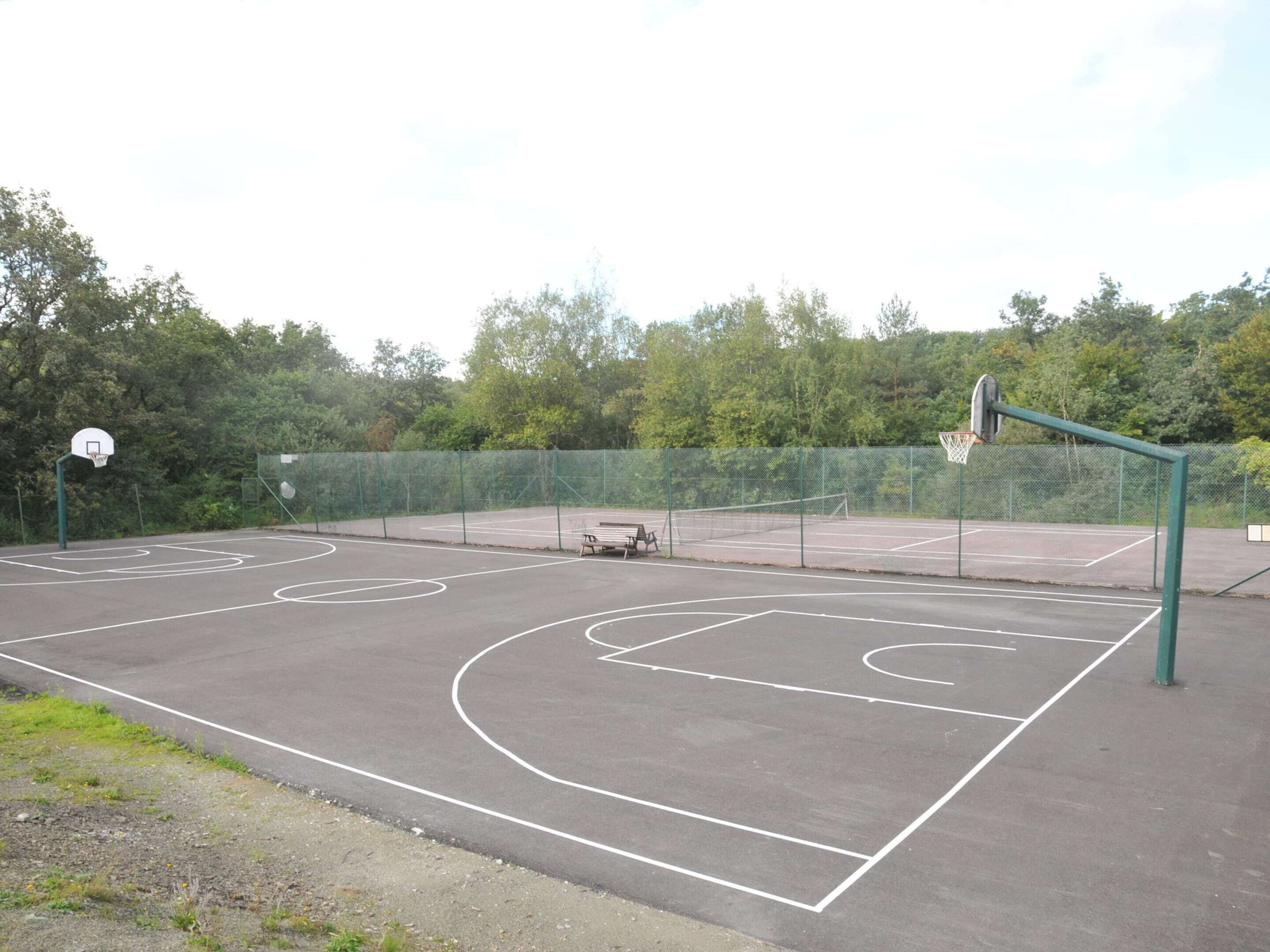 An outdoor basketball court with a green fence, a bench, and trees in the background.