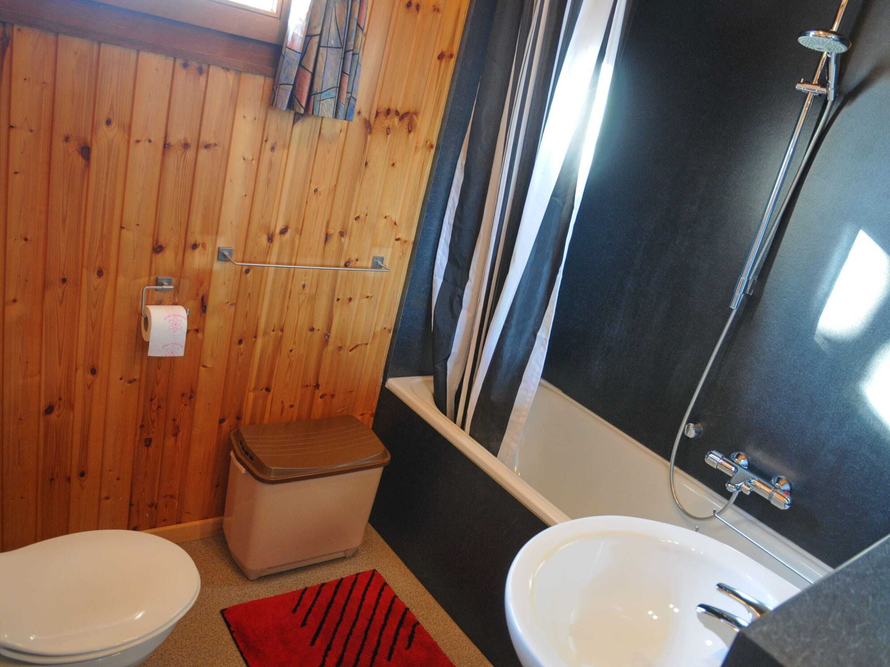 Une petite salle de bain avec un mur en bois, des toilettes, un lavabo et une douche.
