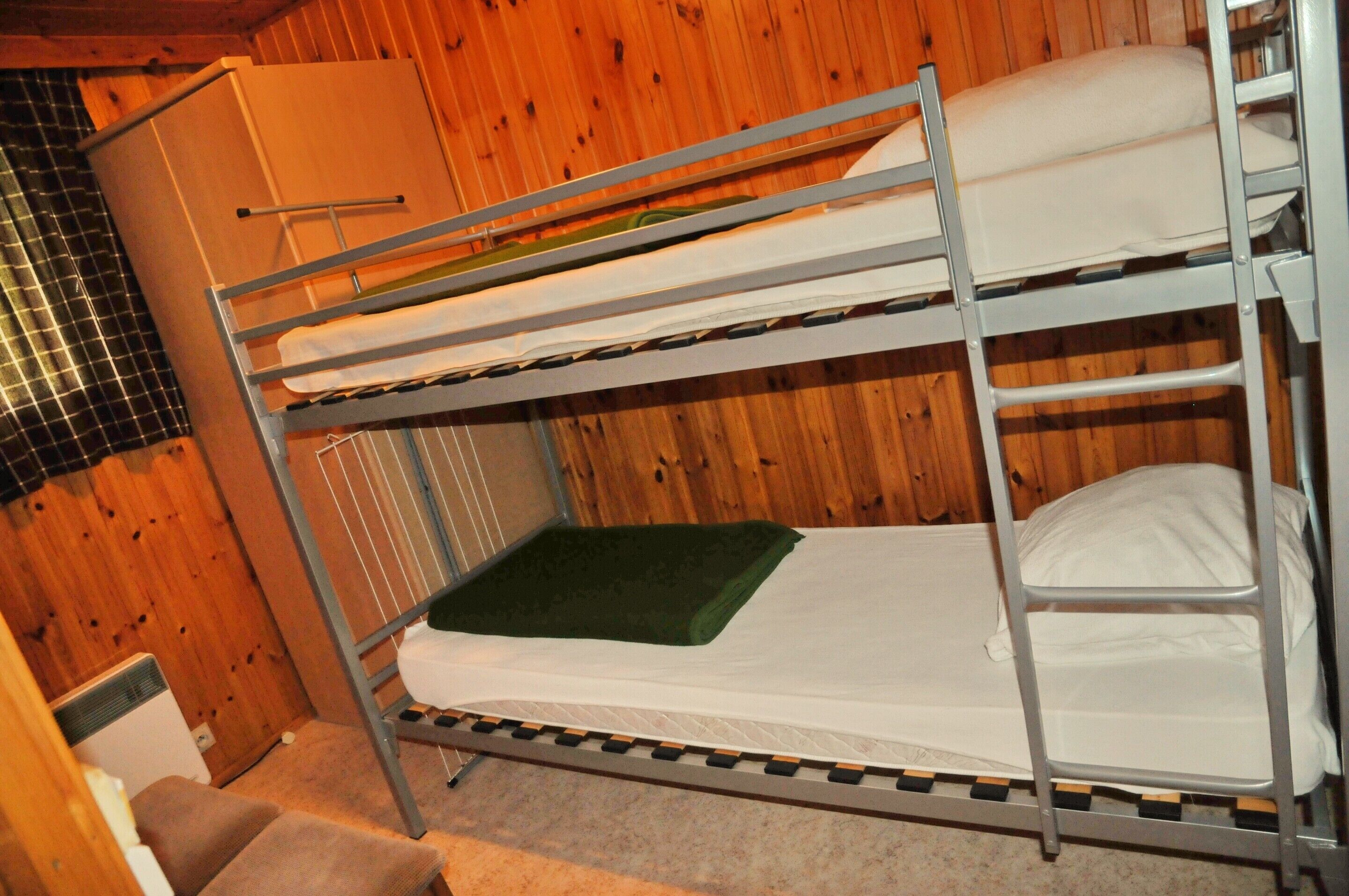 Una cama litera con un colchoneta verde, un armario blanco y un calentador.