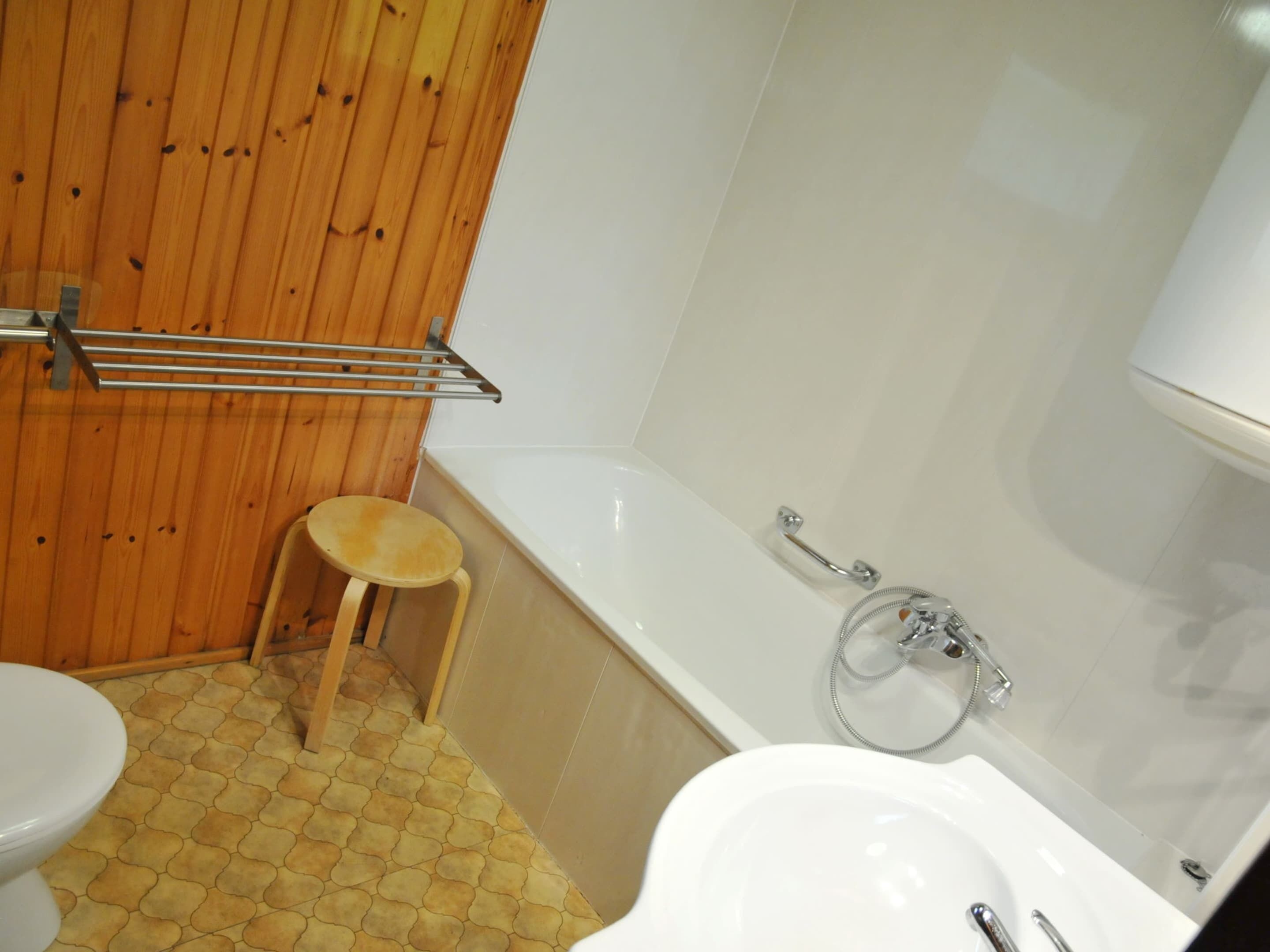 A bathroom with a wooden floor, a white bathtub, a white sink, and a wooden stool.