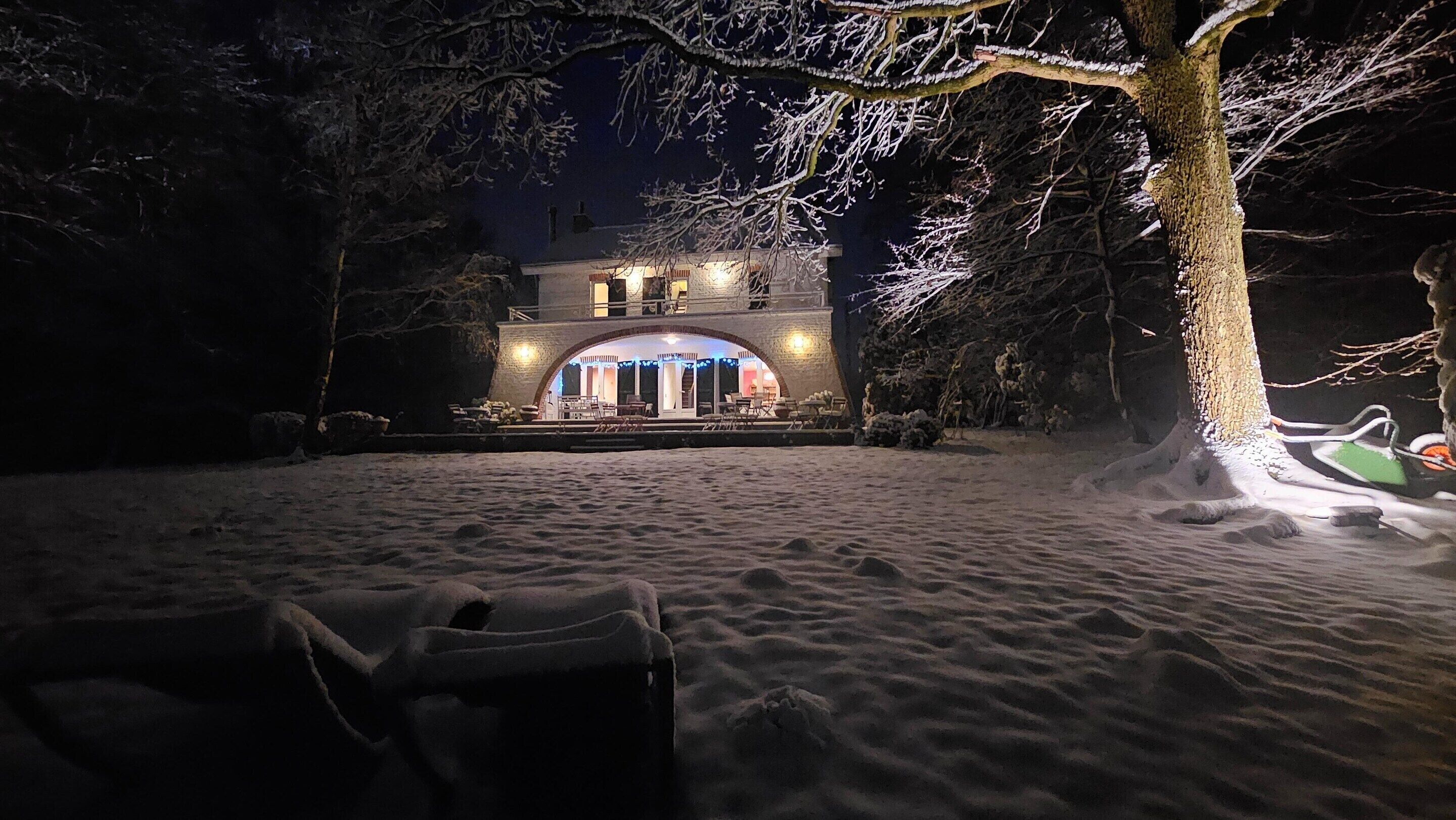 Een gebouw met twee verdiepingen en een overdekt terras, omringd door besneeuwde grond en bomen.
