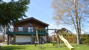 A wooden house with a balcony, a wooden swing set, and a slide in the yard. - Longfaye Chalet With Sauna (Malmedy)
