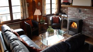 A cozy living room with a leather sofa, a glass coffee table, a fireplace, and a television mounted above the fireplace. - Longfaye Chalet With Sauna (Malmedy)