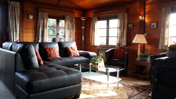 A cozy log cabin interior with a leather sofa, a glass coffee table, and a rustic fireplace. - Longfaye Chalet With Sauna (Malmedy)