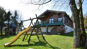 A playground with a slide and swings, a stone oven, and a building with a balcony. - Longfaye Chalet With Sauna (Malmedy)