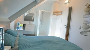 A bedroom with a bed, a bedside table, a lamp, a mirror, a bathroom with a shower, a towel rack, and a wall with decorative stones.