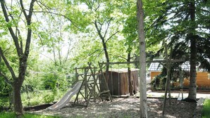 A playground with a slide and climbing structures, surrounded by trees and a wooden shelter.