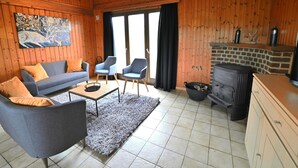 Un salon chaleureux avec des murs en bois, un canapé, deux fauteuils, une table basse et une cheminée.