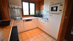 Une cuisine avec des meubles blancs, une hotte de cuisinière en acier inoxydable, un four à micro-ondes et une fenêtre avec des stores.