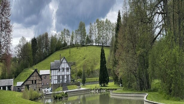 Un bâtiment traditionnel doté d’un toit en pente, situé au bord d’un étang paisible, et entouré d’une végétation luxuriante et d’arbres.