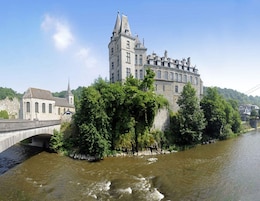 A historic building with a prominent tower, situated beside a river with a bridge in the foreground.