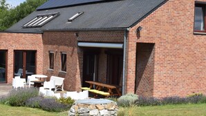A brick house with a patio area featuring outdoor furniture and a stone fire pit. - Villa in Belgium With Private Pool & Garden (Gesves)